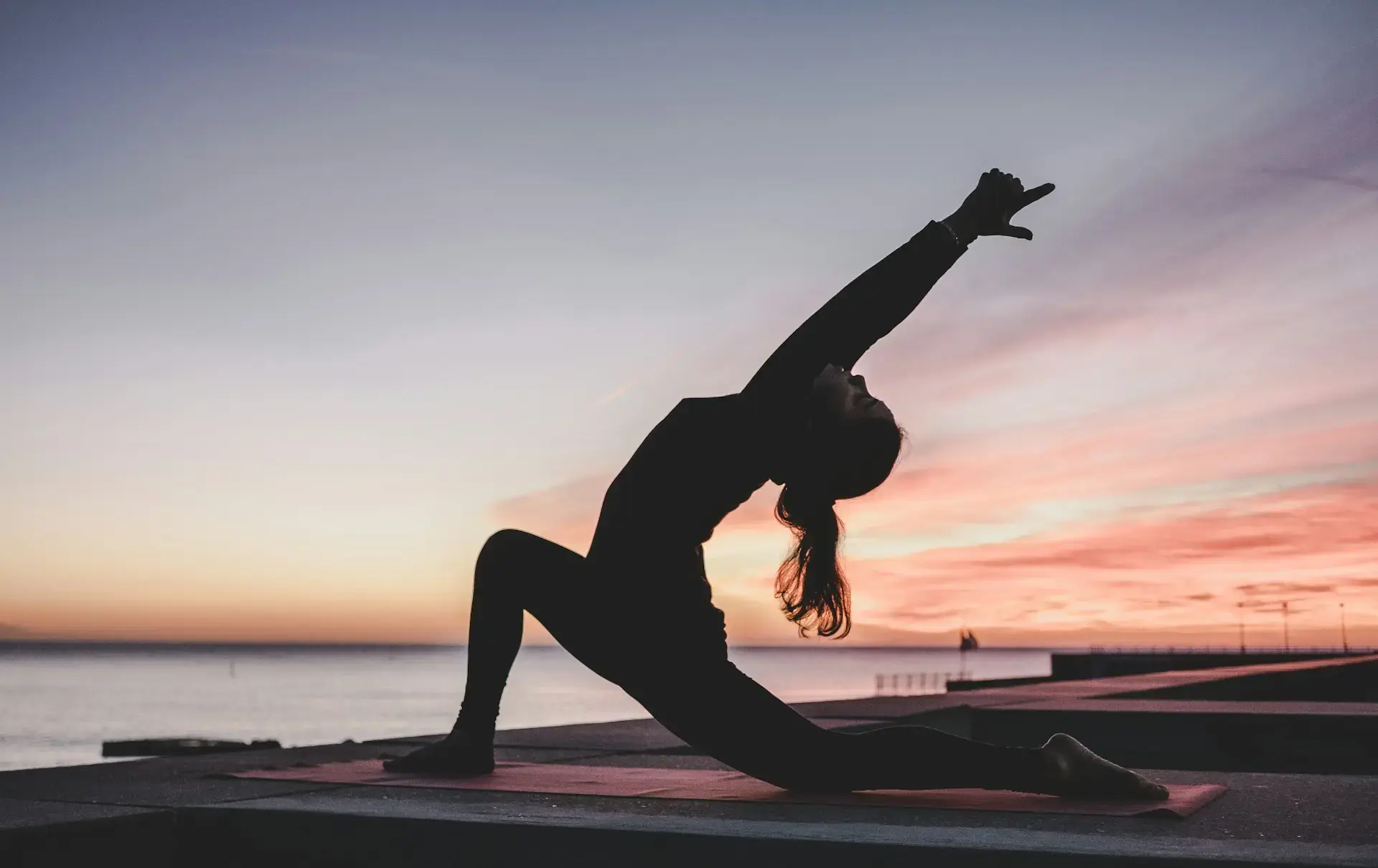 Silhouette of a woman in a backbend yoga pose against a sunset over the water
